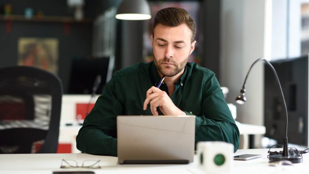Prepare in time A man in a dark green shirt sitting in front of a laptop and thinking.