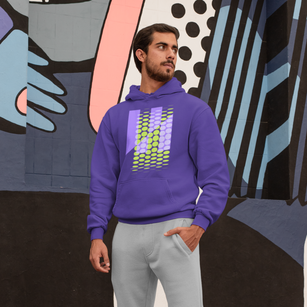 A man in a purple hoodie with an abstract print standing in front of a graffiti.