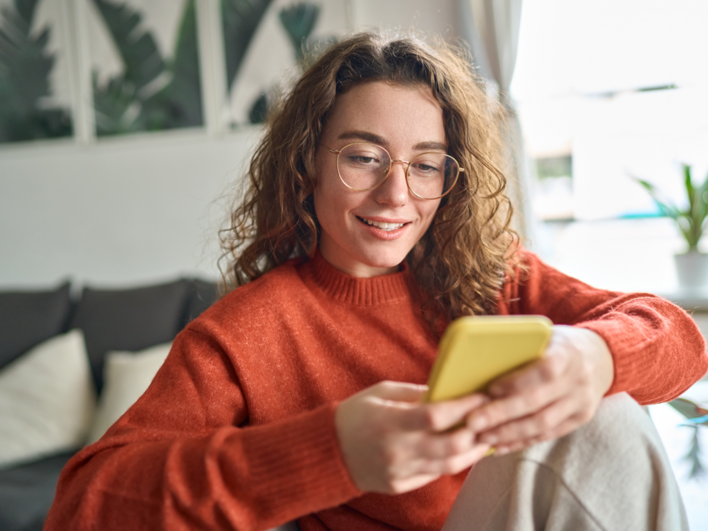 Make your site mobile friendly A woman in glasses is focused on her phone, exploring a mobile-friendly site with interest.